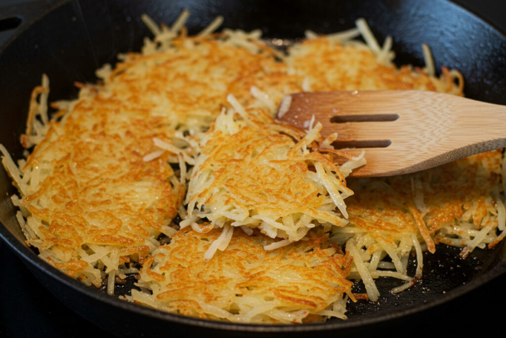 A close-up of shredded hashbrowns being sautéed in a skillet until golden and crispy.